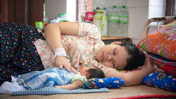 A woman lies next to her newborn child, touching its chest.