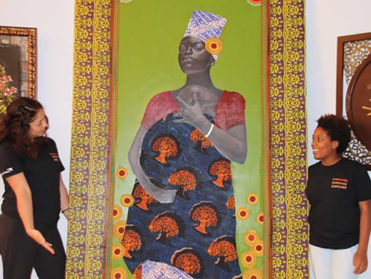 Artists Lauren and Sungi standing next to their masterpiece of a woman wearing Tanzanian traditional clothing.