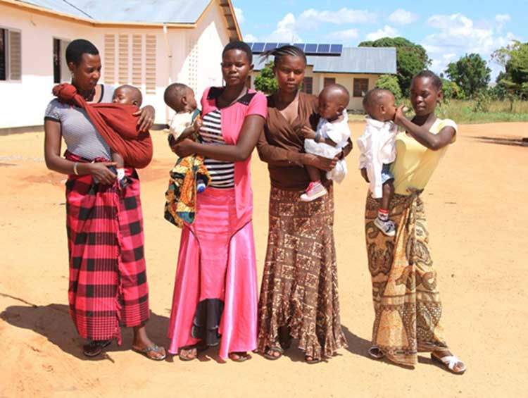 Four women standing next to each other, each carrying their babies.