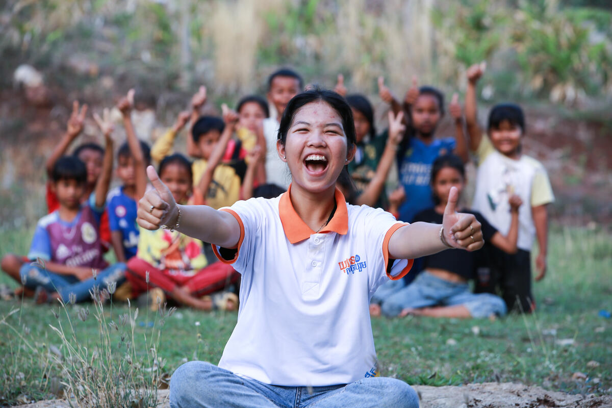 A youth club leader from Cambodia in front of the youth group with a thumbs up gesture