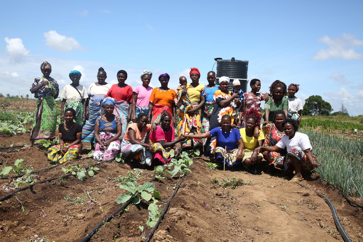 Twenty women and two children pose for a photo in a field of vegetables.