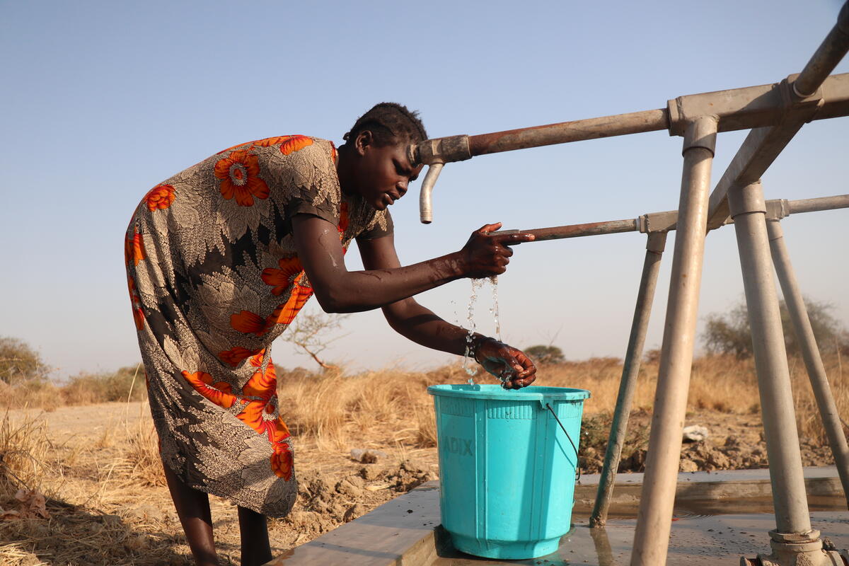 A woman fills a blue bucket with water from a tap. 