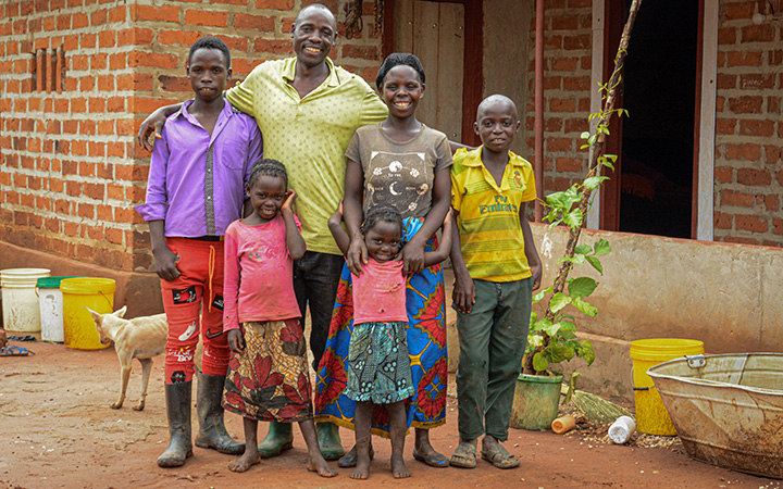 A family in Zambia stands outside their brick house.