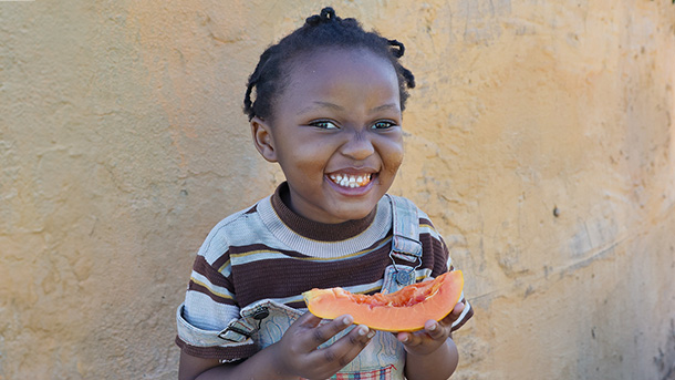 Young girl smiles while holding a papaya fruit.