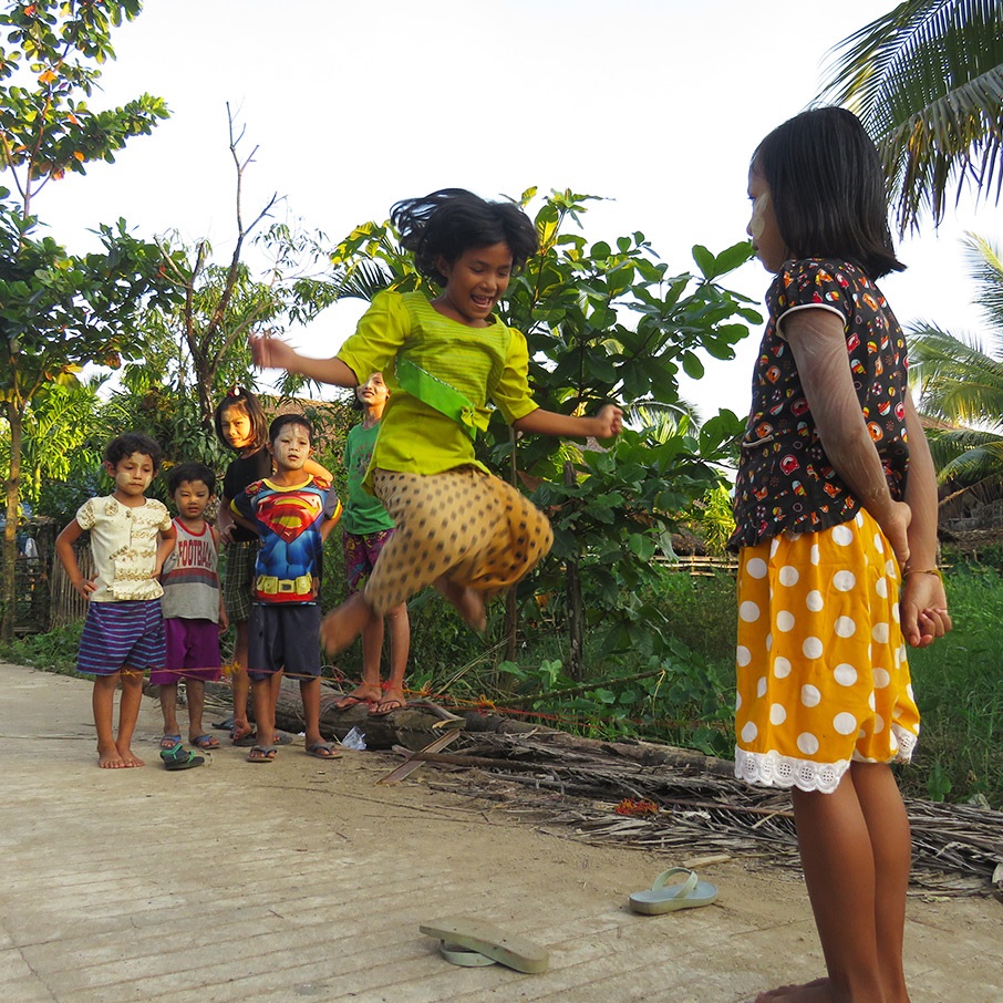 A girl jumps while playing with other children on the street.