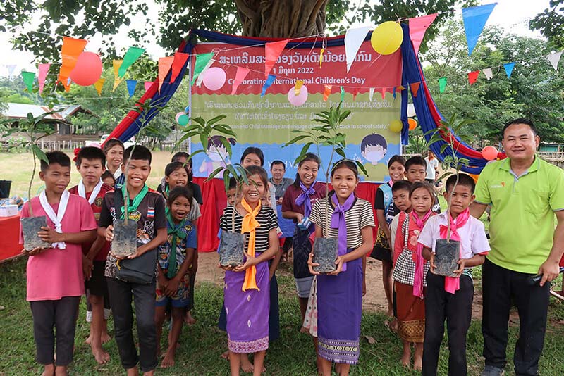 A teacher and his students stand in front of a banner as some students hold saplings for planting. 
