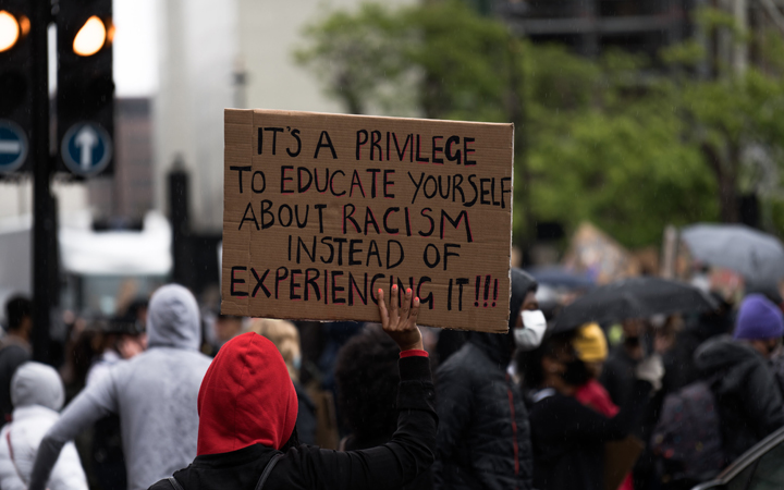 A person holds a sign reading “It’s a privilege to educate yourself about racism instead of experiencing it!”