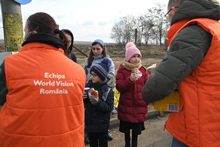 staff in orange vests distribute food rations to children.