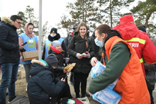 a woman in an orange vest distributes food rations to a child and adults.