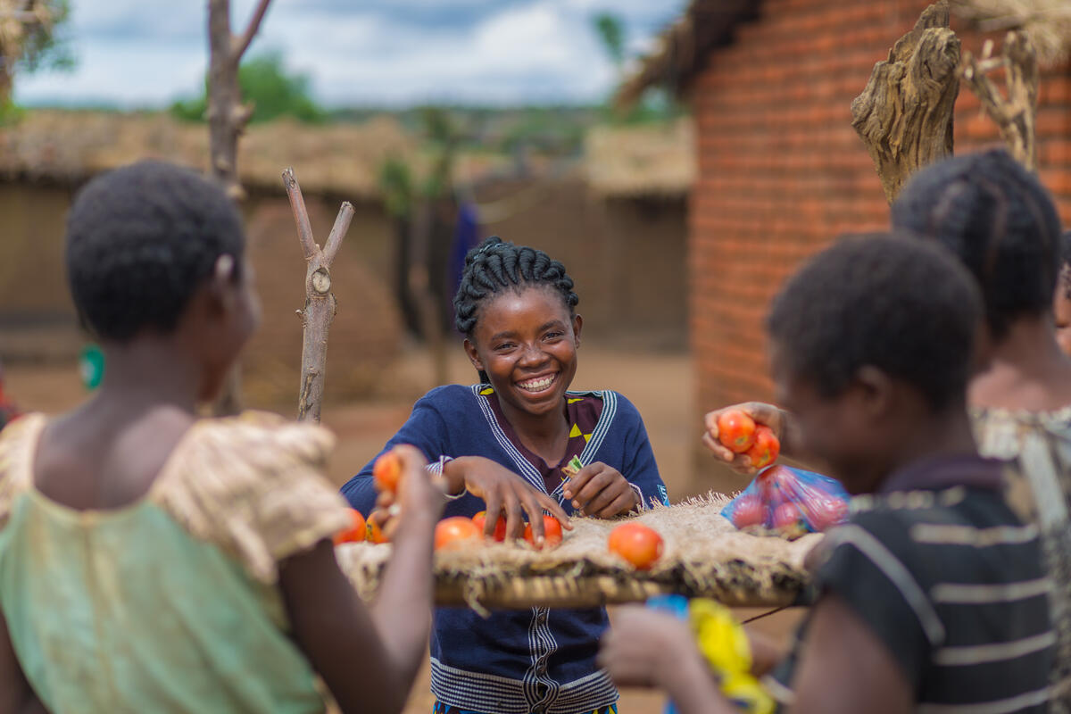 A girl smiling while she sells tomatoes.