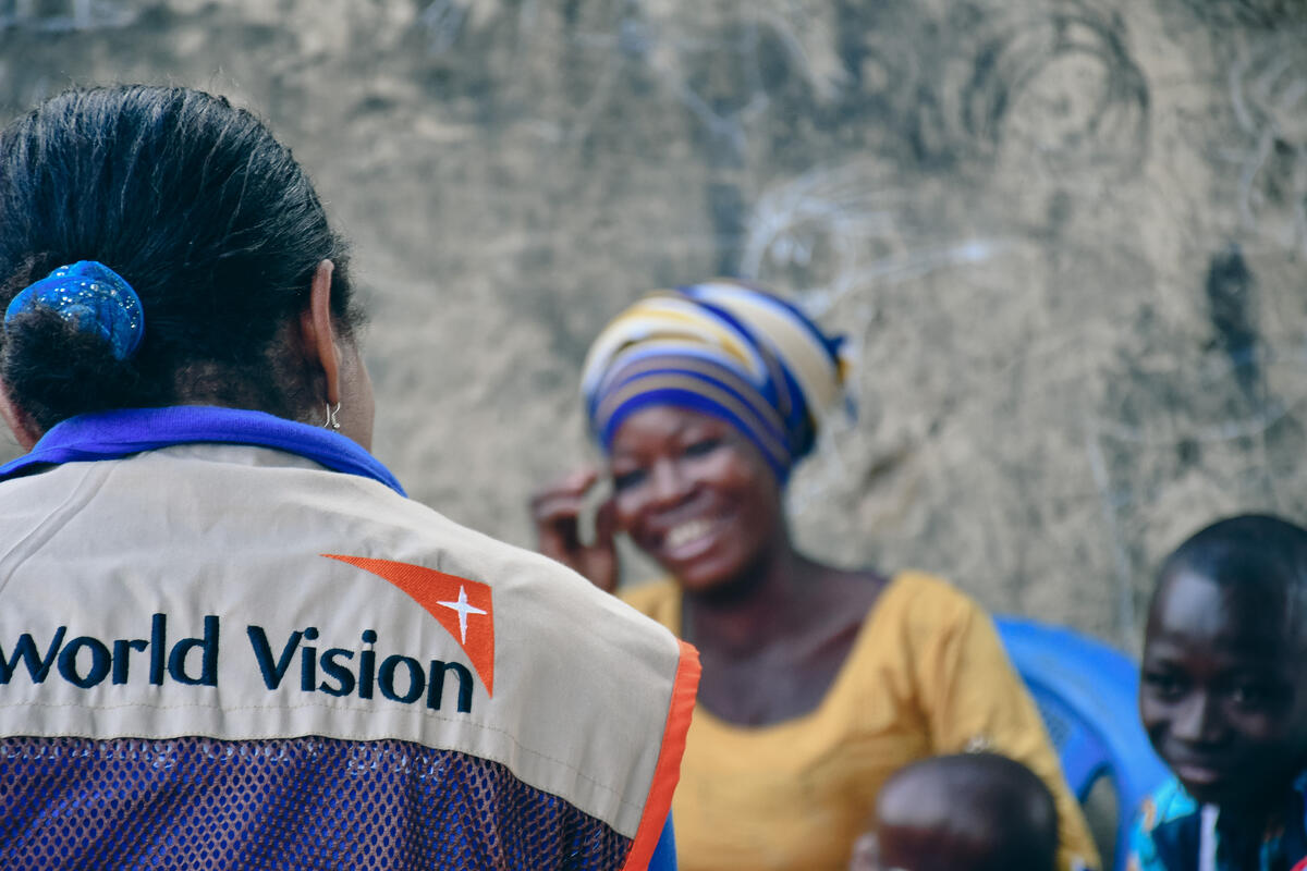 A women smiles at another women wearing a World Vision branded vest.
