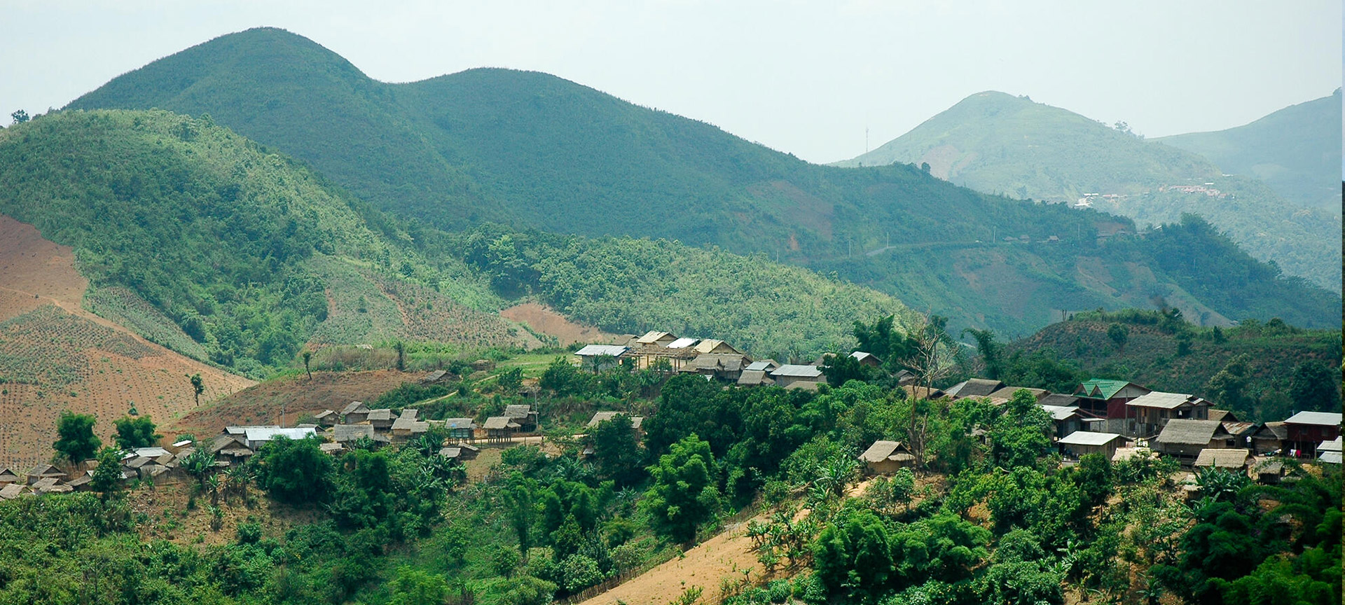 Green hills and mountains surround a few small brown homes. 