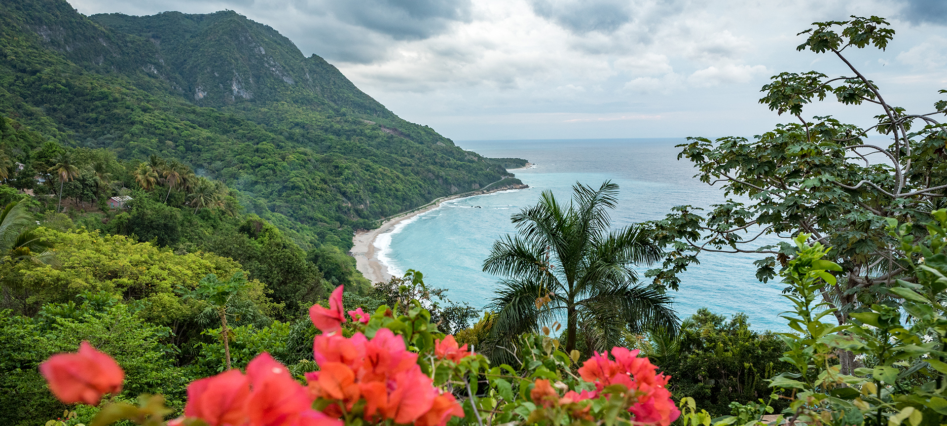 A beautiful view of lush green mountains meeting a sandy beach and bright blue waters