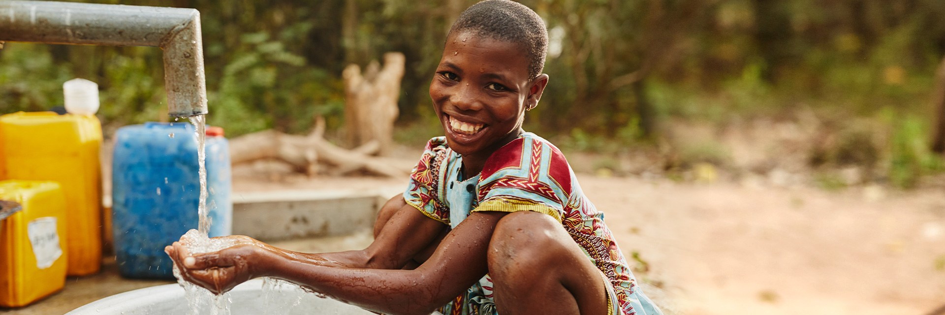 A boy smiles as he shows how he washes his hands in clean water.