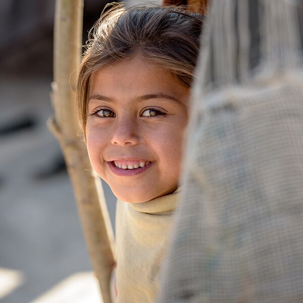 A sponsored child smiling from behind a piece of fabric.