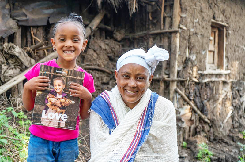 A young girl and her mother smiles at the camera while holding a gift catalogue with her picture on it