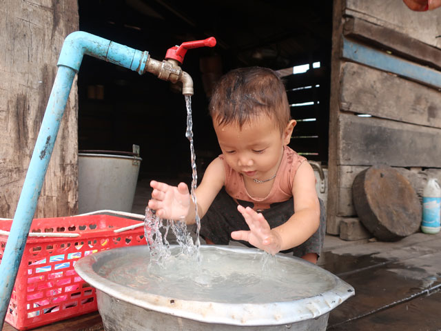 A small child plays with a basin filled with clean water from a faucet right outside his house.