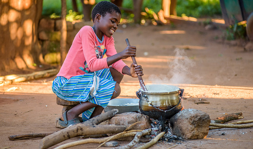 A young girl in Zambia stirs a pot on an outdoor fire