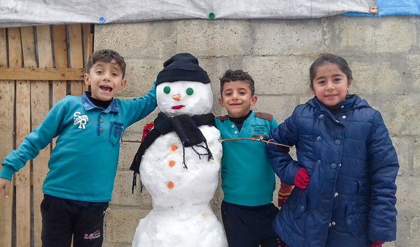 Three Syrian children pose next to the snowman they built