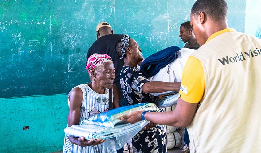 An elderly Haitian woman accepts relief aid items from a World Vision worker at a distribution site for Hurricane Matthew survivors