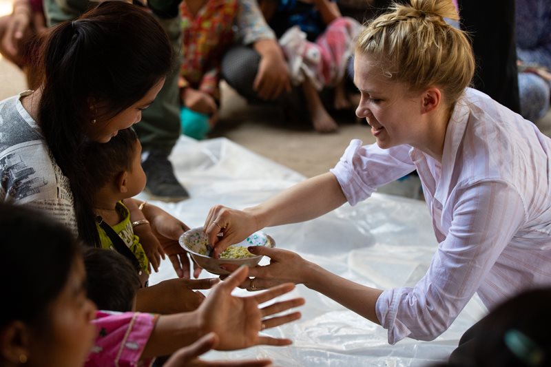 World Vision Ambassador Kaitlyn Weaver helps feed a child who is sitting on his mother's lap.
