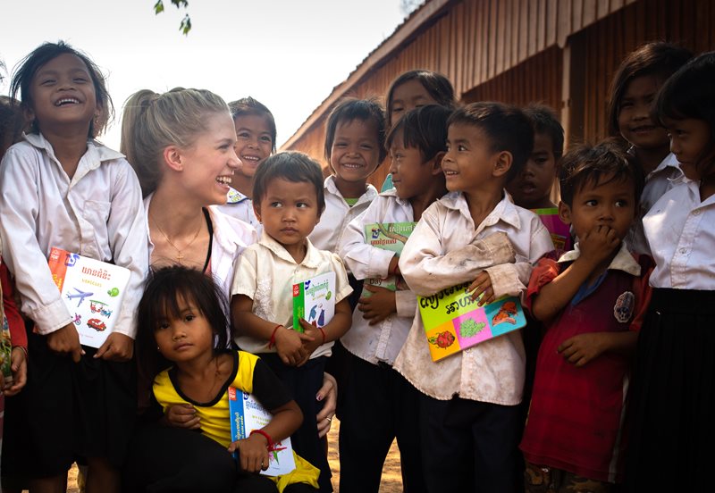 A group of young children from Cambodia smile and laugh around World Vision ambassador Kaitlyn Weaver.
