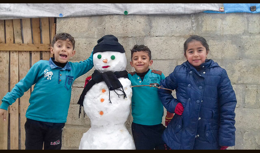 three children smile with a snowman wearing a hat and scarf