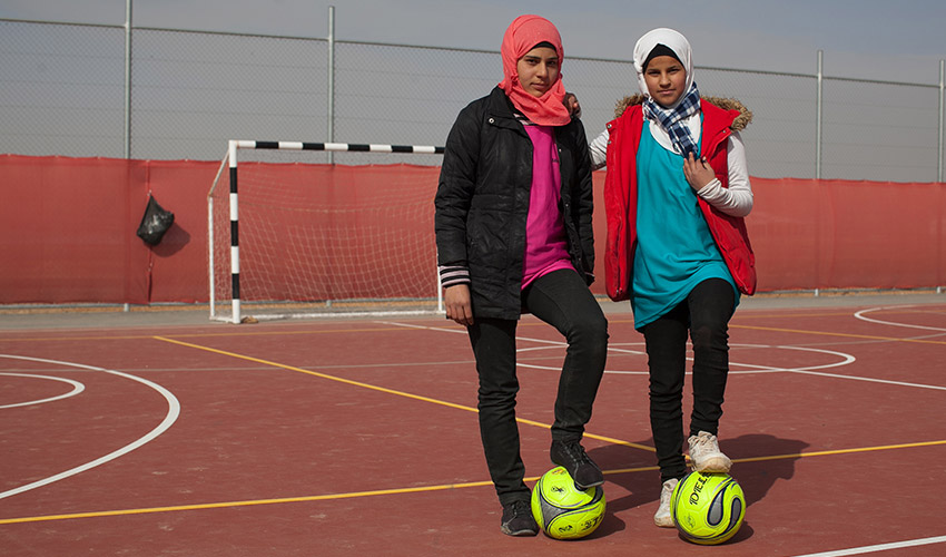 Two young women who are soccer coaches in a Jordan refugee camp stand with a soccer ball