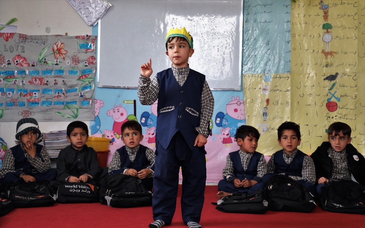 A boy stands in front of his classroom as he presents.