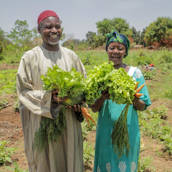 A man and woman in Central African Republic smile while holding vegetables.