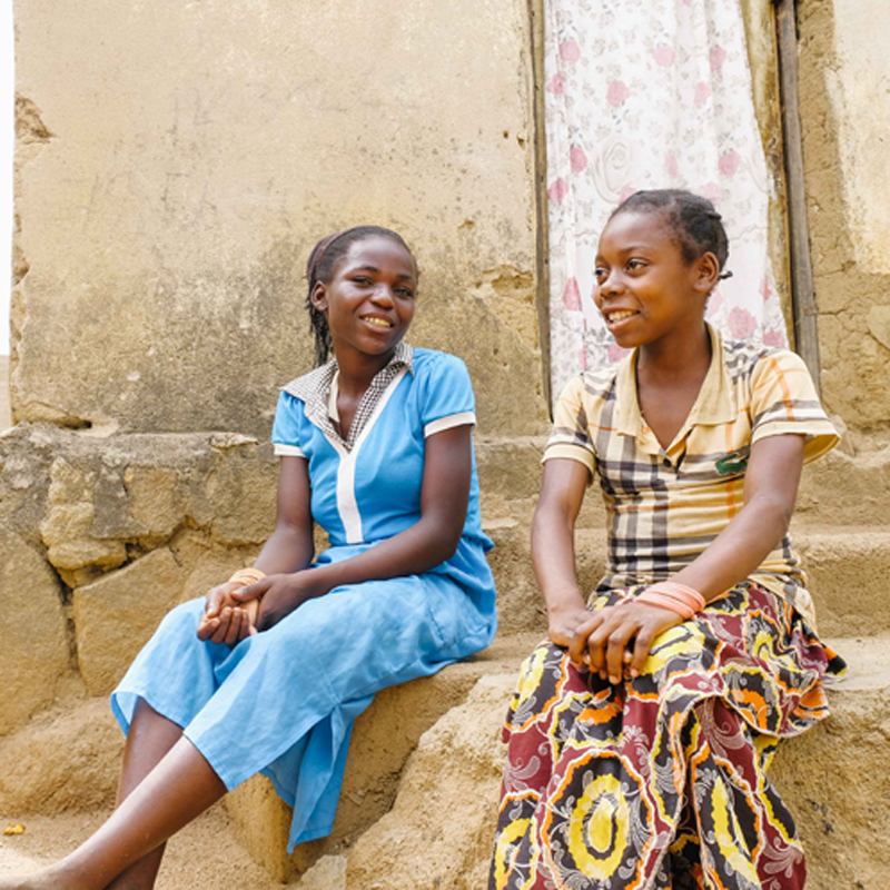 Two girls in Central African Republic sit outside a building.
