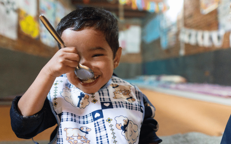 A young Nepalese boy spoons some food into his mouth.
