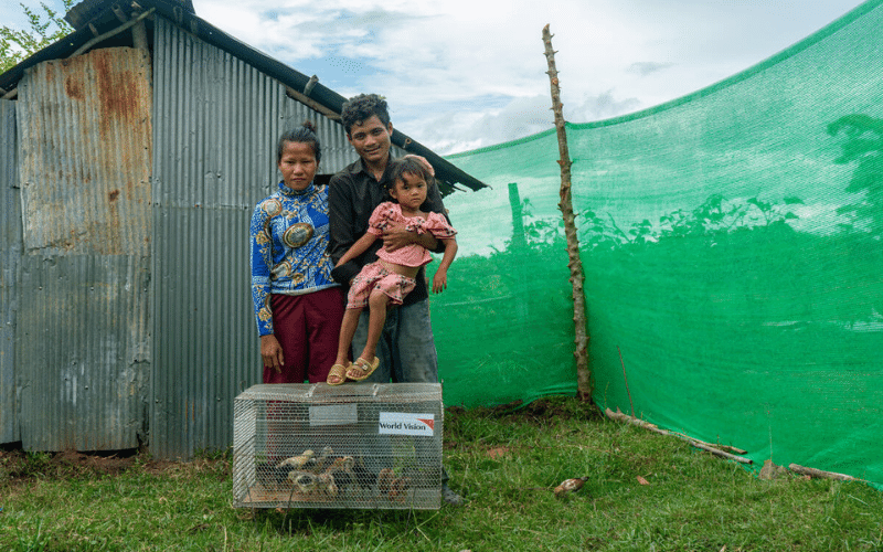 Vichet and his family smile together with their crate of chickens at their feet.