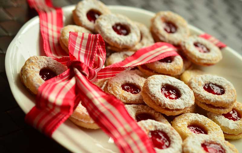 A white plate of sandwich cookies with red jelly centres is adorned with a red plaid bow.