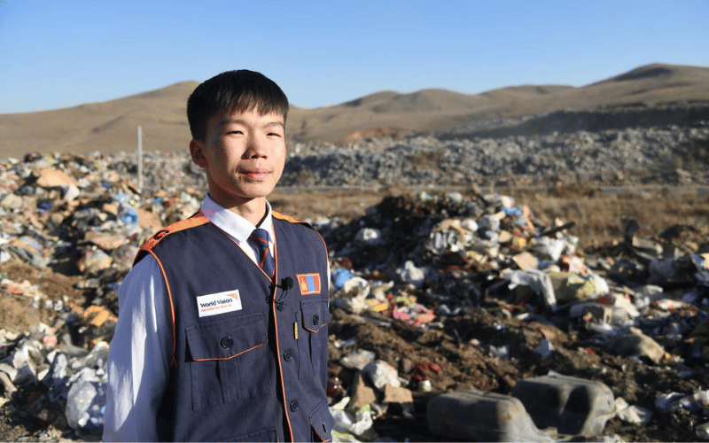 Tulgaa, a Mongolian boy, stands in front piles of garbage.