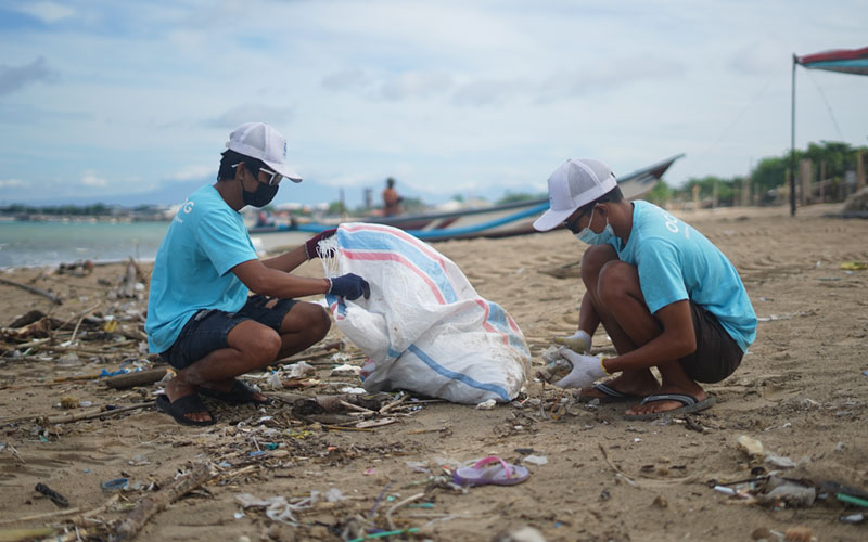 Two men from The Ocean Clean-up Group in Bali, Indonesia crouch down to pick up garbage along the beach.