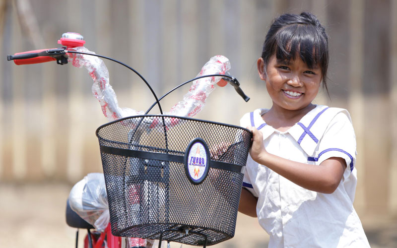 A young girl smiles as she holds a brand-new bicycle.