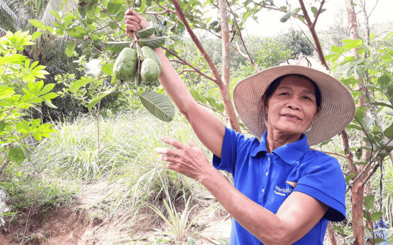 Huong holds one of the branches of her jackfruit tree, showing its fruit.