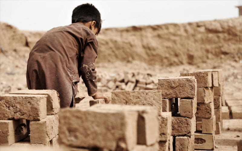 A boy places a heavy brick on a pile.