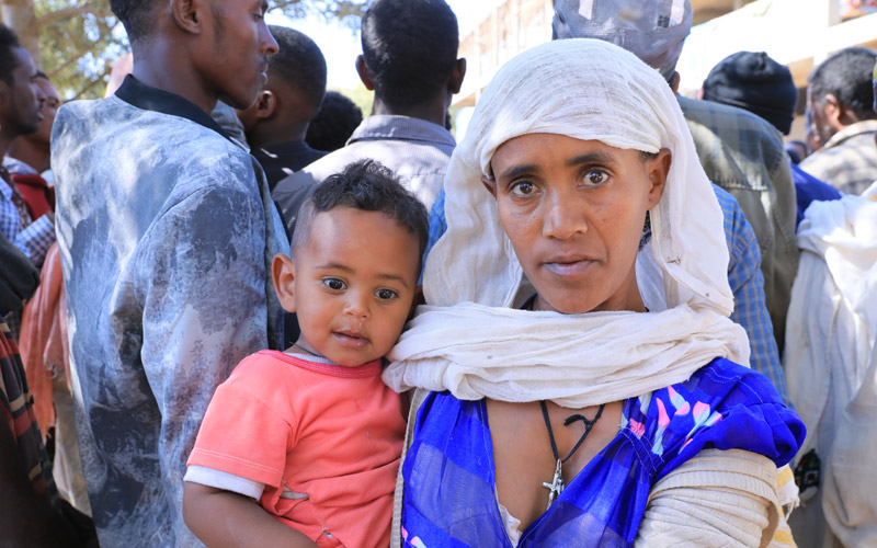 an Ethiopian woman stands holding a baby.