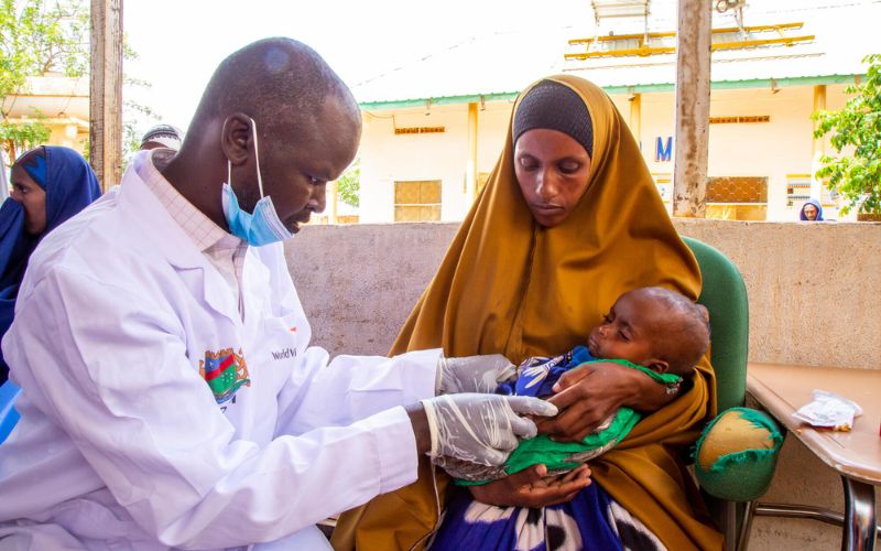 A World Vision clinic staff examines a young child resting in their mother’s arms.