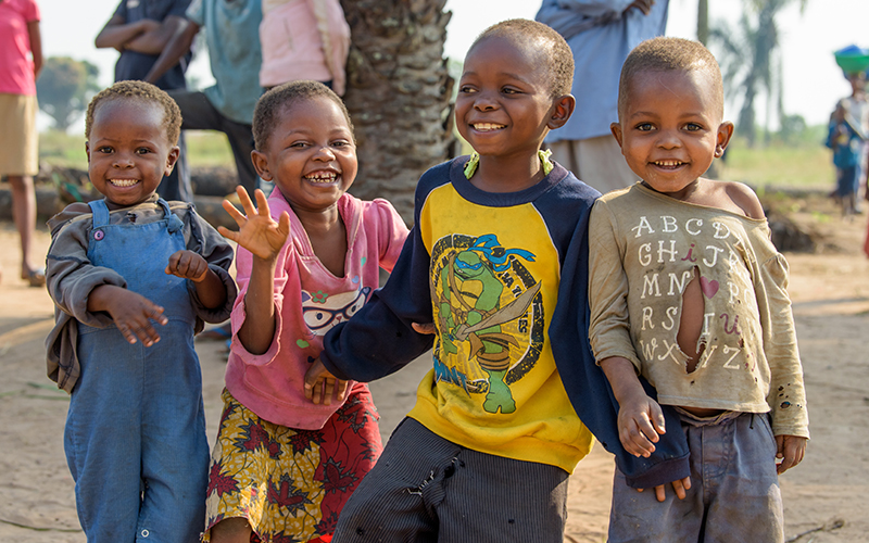 Four young children from the Democratic Republic of Congo playfully smile and wave at the camera.