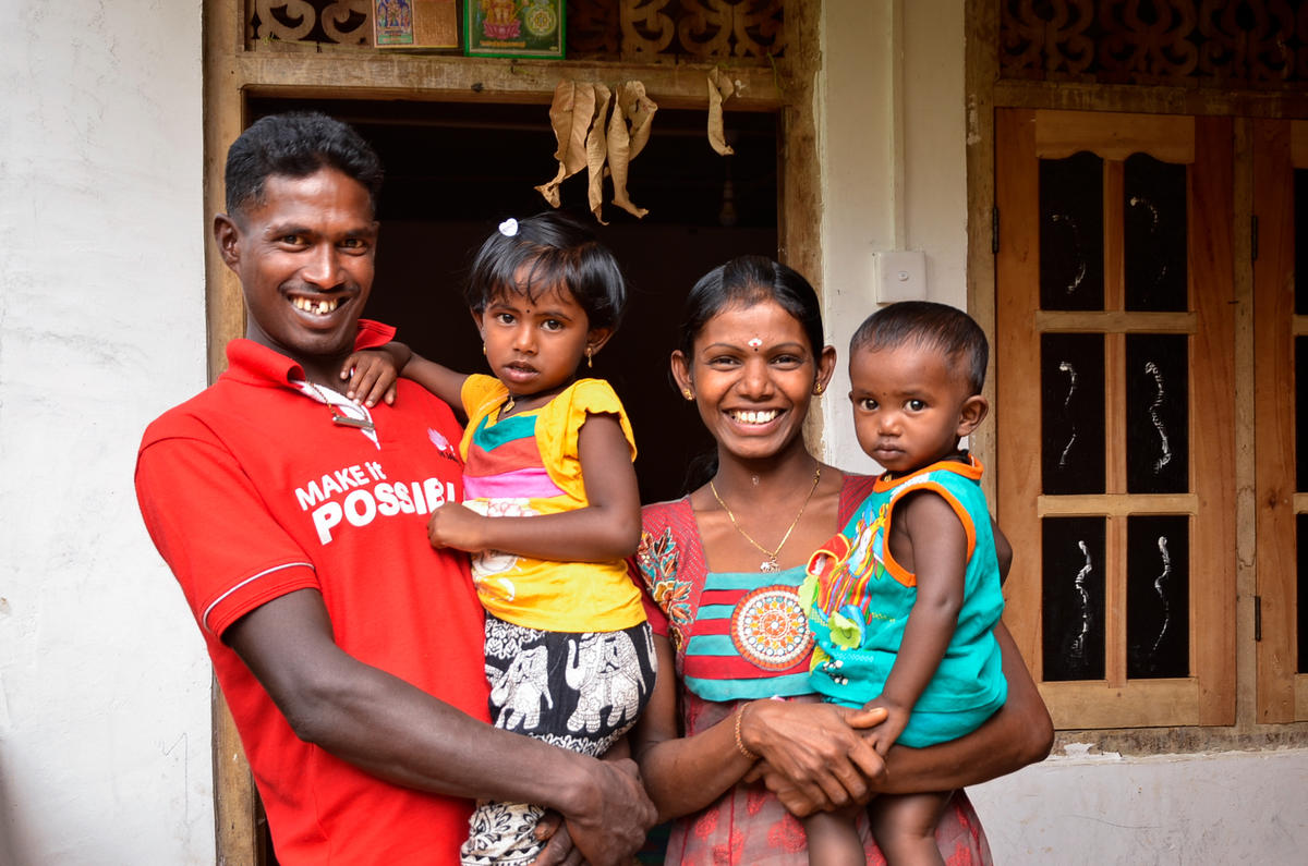 A wife and husband in Sri Lanka hold their two children in their arms and smile for the camera.