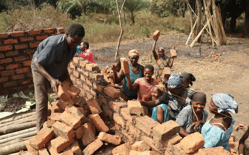 A crowd of excited South Sudanese women carry bricks to the foundation of a new building.