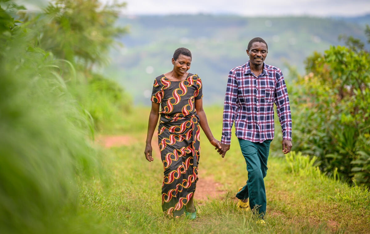 A woman and a man hold hands as they stroll along a grass-covered path in Rwanda.