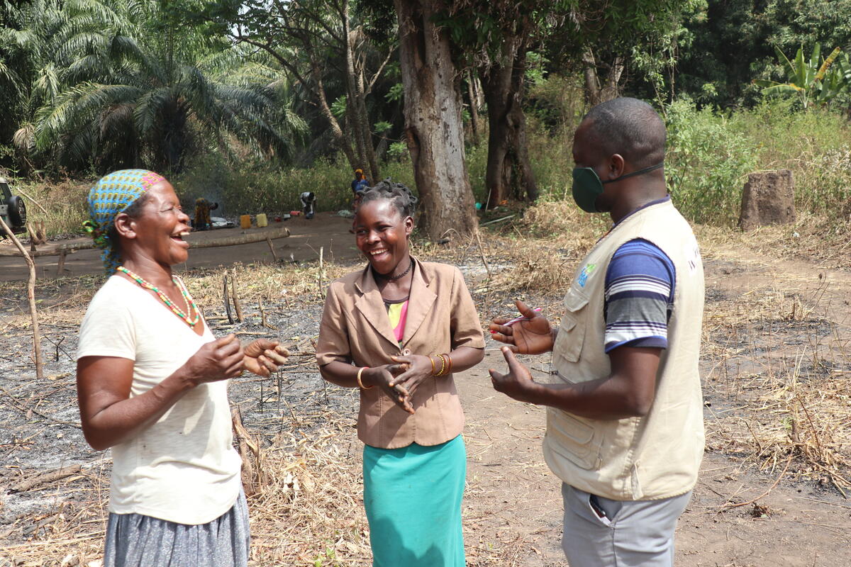Two women smile and laugh as they stand in a clearing while talking to a World Vision worker.