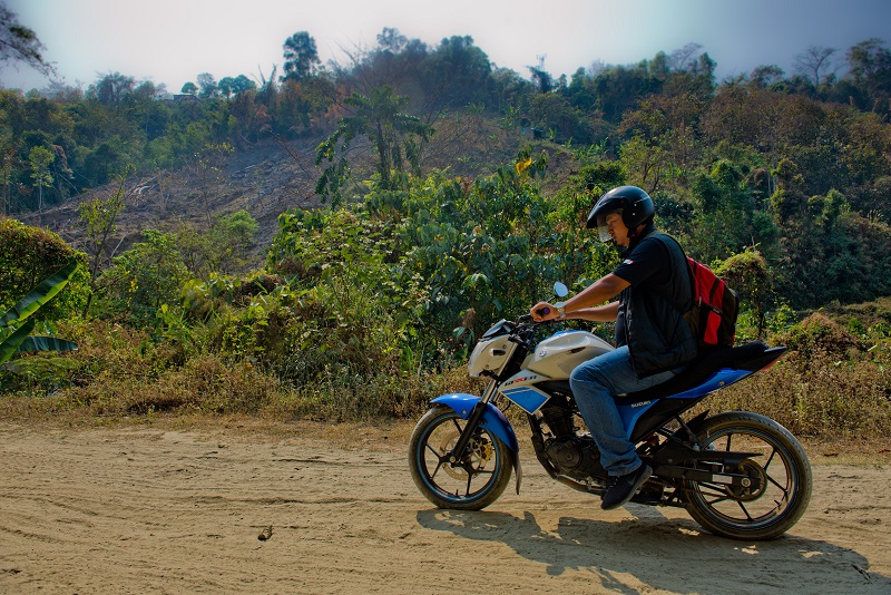 A man on a motorcycle travels through lush green forest.