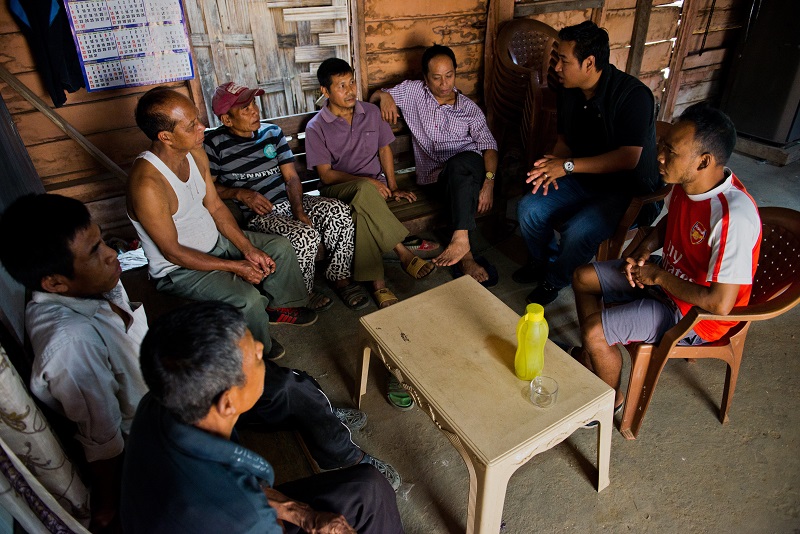 A humanitarian sits with a group of farmers at a small table.