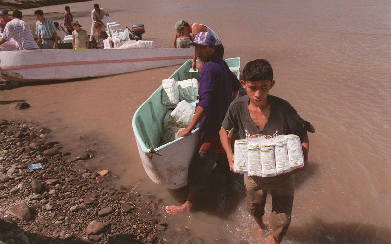 A boy carries provisions from a small boat to the shore.
