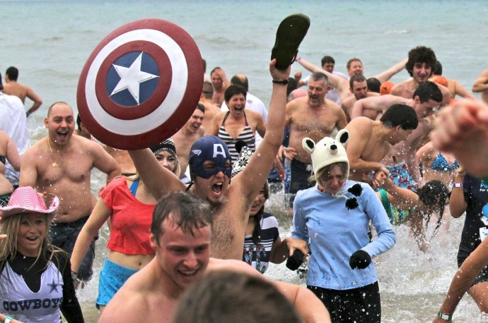 A crowd in swimming suits run out of a cold lake while a guy with a Captain America shield celebrates.